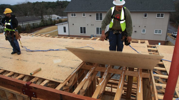 Construction site using the DryMax High Performance OSB Sub-floor product. Construction worker in green vest & white hard hard is laying down the sub-flooring