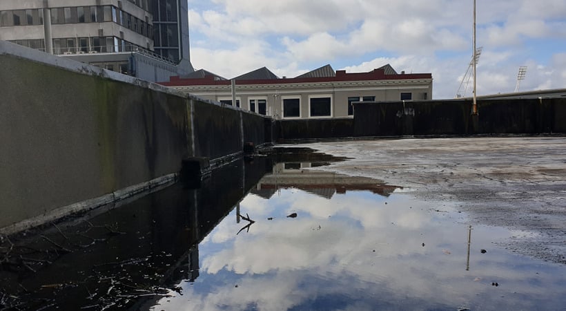 Clouds are reflected in water pooling on a portion of a low-slope commercial roof.