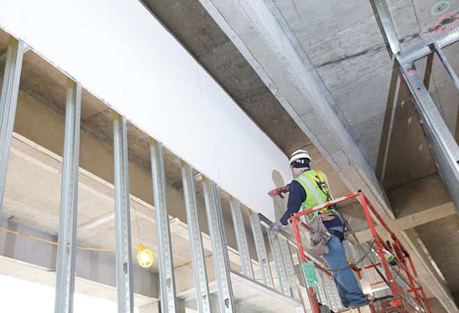 Construction worker installing DensArmor Plus® fiberglass mat gypsum panels on interior wall framing.