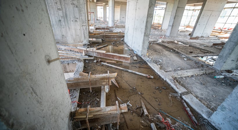 The aftermath of a flooded commercial building, gutted down to the concrete, load-bearing walls, with debris littering the floor.